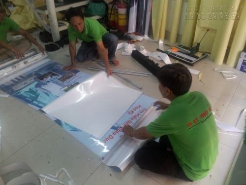 Nhân viên gia công của In Kỹ Thuật Số gắn poster PP vào banner cuốn (giá cuốn) cho trưng bày