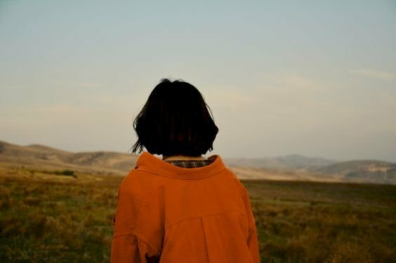 Hình ảnh cô gái tóc ngắn quay lưng đi bộ dưới đồng cỏ xanh