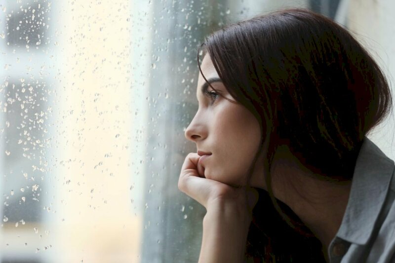 Cô gái xinh đẹp ngồi ngắm mưa bên cửa sổ với tâm trạng buồn