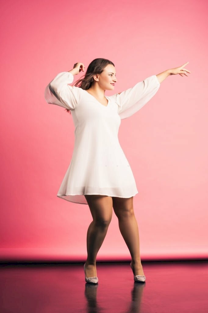 Tạo dáng chụp ảnh dành cho người mặt béo tuyệt đẹp và nghệ thuật với tư thế đứng nghiêng người, mặt quay ngang, tay dơ cao tạo dáng, miệng cười tươi