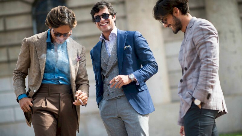 Cách tạo dáng nam với 3 bộ vest khác nhau đang trò chuyện trên phố, với 2 người tay cầm điếu thuốc, tay còn lại đặt ở túi quần, người còn lại trong bộ vest xám miệng mỉm cười đầu hơi cúi