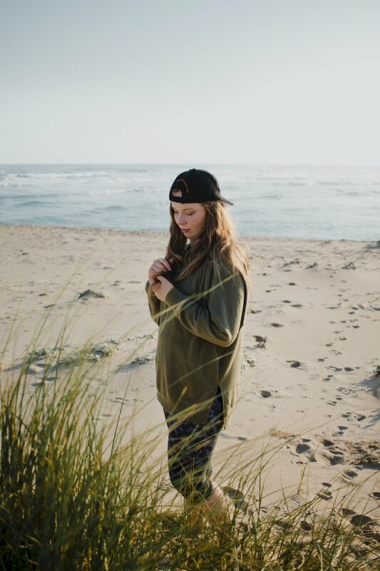 Tạo dáng chụp ảnh ngoại cảnh e thẹn trên bãi cát trắng, 2 tay nắm đuôi tóc cùng chiếc mũ lưỡi trai đội ngược, mắt nhìn xuống