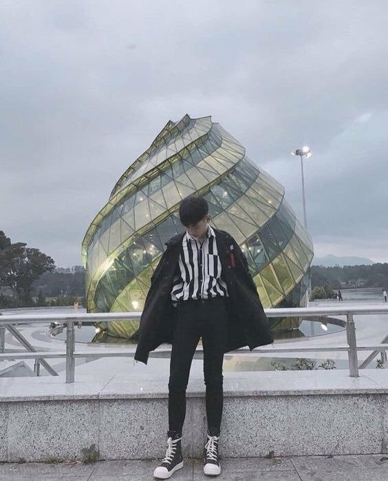 Kiểu tạo dáng thần thái ngút ngàn cho thanh niên với phong cách khóa áo lên vai, đầu hơi cúi, mắt nhìn xuống đất, ngồi tựa người và khung sắt