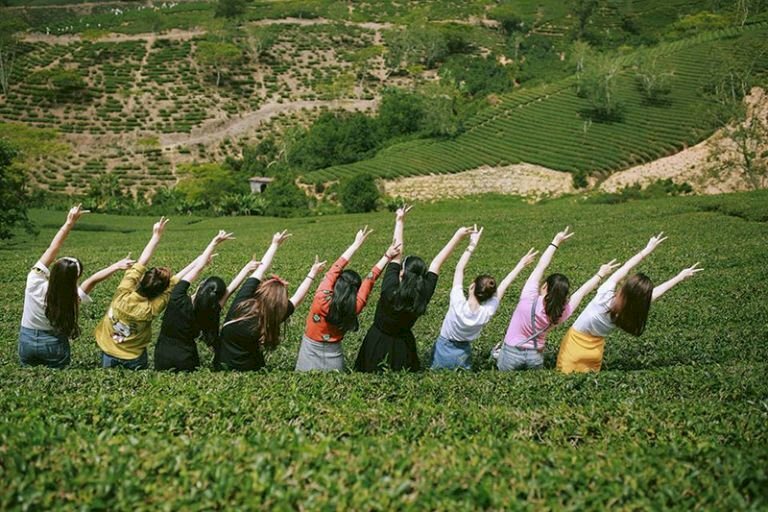 Cách tạo dáng chụp ảnh trên đồi chè cùng nhóm bạn hài hước với dáng đứng hơi nghiêng một bên, 2 tay dơ cao "say hi", góc chụp lấy từ sau lưng