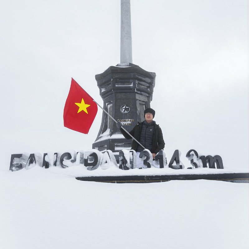 Tạo dáng chất lừ với 2 tay cầm cờ Tổ Quốc trên đỉnh Fansipan dưới trời mùa Đông tuyết phủ trắng xóa thể hiện sự mạnh mẽ và ý chí