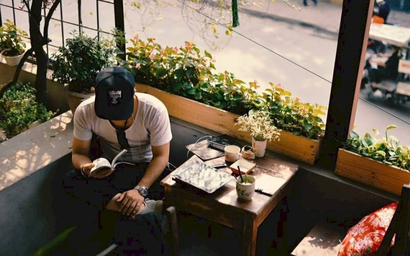 Tạo dáng nam chụp từ trên xuống với dáng ngồi gác chân chữ ngũ, 1 tay cầm sách, 1 tay đặt lên chân