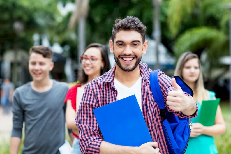 Tạo dáng thần thái cho nam tại sân trường với miệng tươi cười, vai mang balo kết hợp với hiệu ứng làm mờ cảnh phía sau tạo điểm nhấn nổi bật cho tấm ảnh kỷ yếu của cá nhân