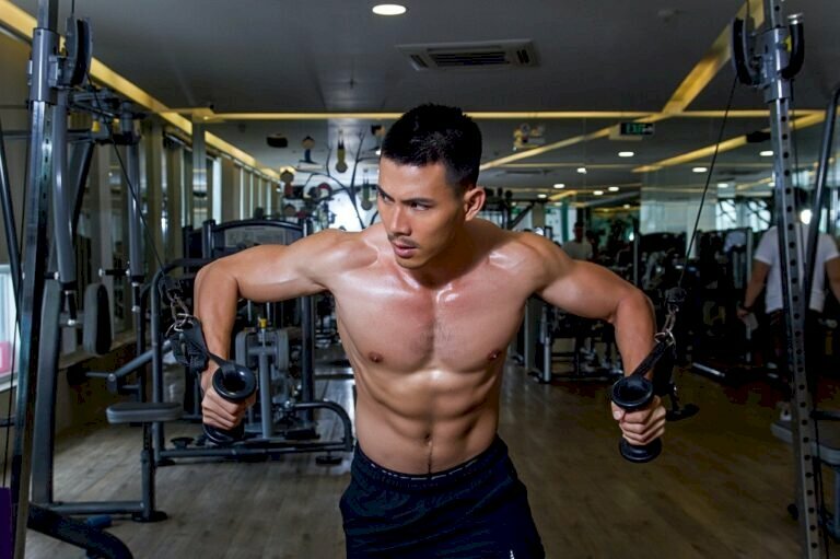 Cách tạo dáng chụp ảnh tập gym khi đang tập kéo cáp với máy tập thể hình, 2 tay cầm tay nắm dây cáp có gắn ròng rọc, tạo tư thế 2 tay dang 2 bên, giống như chim đang bay và phần thân người trên hơi cong về phía trước, dáng này khoe được sức mạnh cơ bắp và tạo được khối cơ ngực nở nang, chắc khỏe, thân hình vạm vỡ.