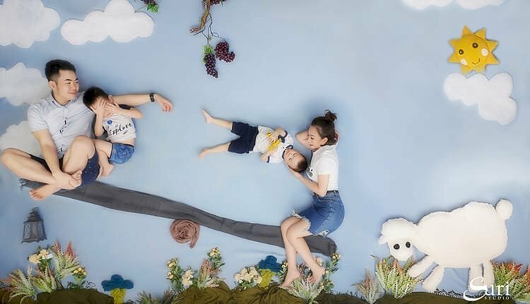 Ý tưởng chụp ảnh gia đình vô cùng độc đáo ảo diệu, tạo ảo giác cho người xem, bằng nền được vẽ hình bầu trời xanh mây trắng, có 1 cái bập bênh, bố mẹ ngồi trên cái bập bênh, 1 đứa con đứng về phía mẹ, 1 con đứng với bố. 