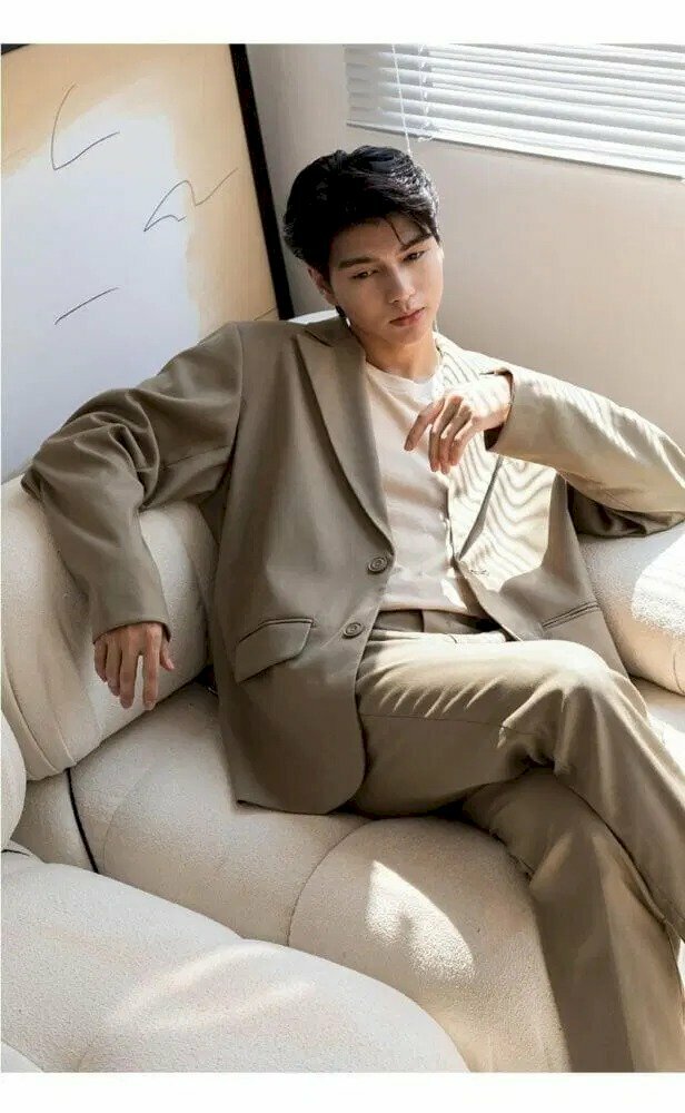 Cách tạo dáng chụp ảnh tết cho nam khi mặc vest theo phong cách Hàn Quốc là có thể ngồi ngả người lên sofa, 2 tay đặt lên thành ghế, chân bắt chéo, và gốc chụp từ trên xuống.