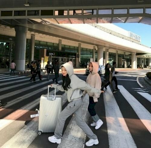 Cách tạo dáng chụp ảnh ở sân bay cho 2 người bạn thân nữ cực kỳ cute dễ thương với dáng đang bước đi qua đường với một bước dài, tay vung mạnh ra sau, người hơi khom lên phía trước, một tay đưa ra trước đẩy vali.