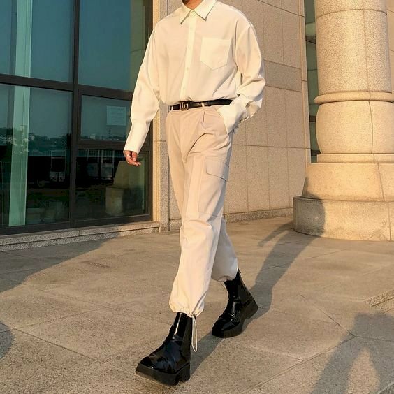 Trang phục phong cách với sự kết hợp của chiếc áo sơ mi trắng gài kính cổ cùng chiếc quần màu be, kết hợp với đôi boot đen giúp bạn nam không bị gầy, và khi tạo dáng chụp ảnh chỉ cần bước 1 chân trước 1 chân sau như đang bước đi, 1 tay để vào túi quần, còn 1 tay thả lỏng là sẽ có một bức ảnh đẹp.