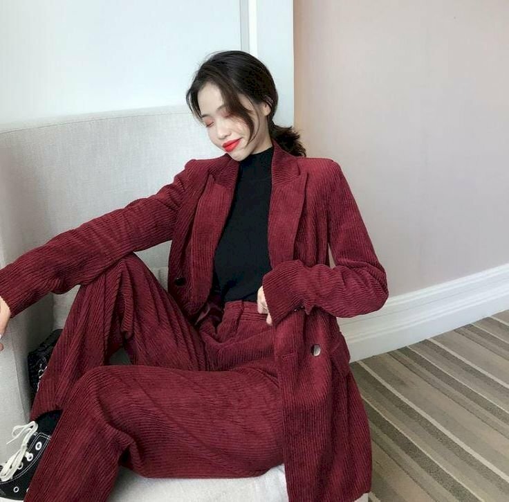 Cách tạo dáng với vest nữ khi ngồi với 1 chân co 1 chân hơi duỗi, 1 tay đặt trên chân co, 1 tay đặt ngay lưng quần, gương mặt hơi cúi xuống, mỉm cười nhẹ. 