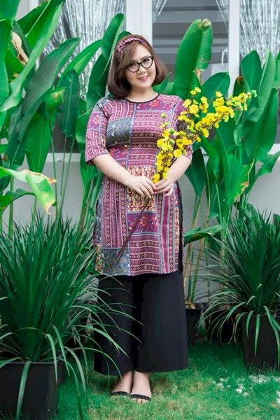 Cách tạo dáng với áo dài Tết cho người béo với đạo cụ là cành hoa mai cầm nhẹ nhàng để phía trước bụng, để che đi khuyết điểm 2 cằm nàng hãy cúi nhẹ đầu nghiêng về 1 bên để giúp cằm trở nên Vline hơn và mặt thon gọn hơn.