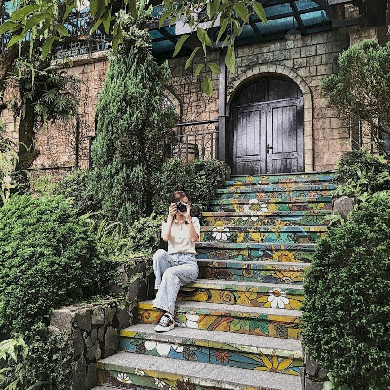 Con đường bích họa với mỗi bậc thang là hình vẽ hoa cỏ tạo thành bức tranh 3D tuyệt đẹp, kết hợp với khung cảnh cổ kính xung quanh, tại đây bạn có thể tạo dáng đang ngồi chụp ảnh, với 1 chân đặt trước 1 chân sau, hai tay cầm máy ảnh đưa lên chụp hình. 