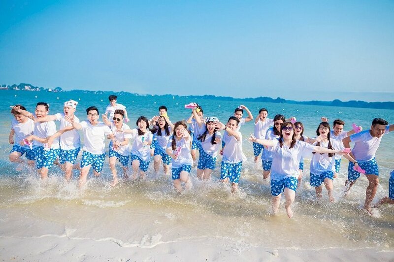 Cách tạo dáng chụp ảnh biển tập thể đơn giản, vui vẻ bằng cách mọi người đứng trên nước và cùng chạy ào lên phía trước, vừa chạy vừa đưa tay lên trước, gương mặt tươi cười vui vẻ.