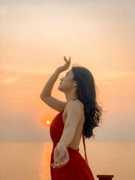 Tạo dáng chụp ảnh bình minh trên biển cho nữ cực đẹp với dáng đứng nghiêng người với ống kính, 1 tay đưa nhẹ về hướng ống kính, 1 tay còn lại đưa cao lên trên mặt.