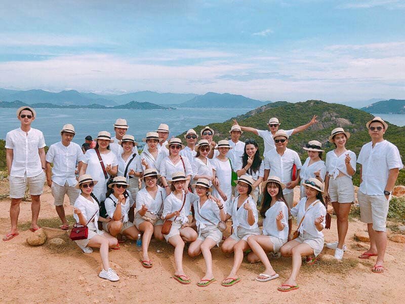 Kiểu tạo dáng chụp ảnh tập thể ngoài trời khi đi du lịch đơn giản bằng cách xếp thành 3 hàng ngang với hàng trước các bạn nữ ngồi xổm trên 1 chân và đưa 1 chân lên phía trước, hai hàng sau mọi người cùng đứng dậy.