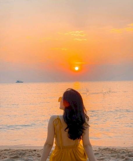 Tạo dáng chụp ảnh bình minh trên biển cho nữ với kiểu ngồi quay lưng về hướng ống kính, với hai tay chống trên cát, người hơi ngã về phía sau, đầu nghiêng qua 1 bên, chụp ảnh lấy trọng ánh bình minh đang lên.