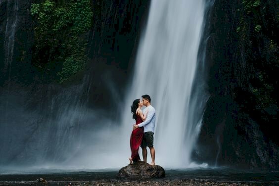 Cách tạo dáng chụp ảnh với thác nước đẹp cho cặp đôi với tạo dáng đứng trên tảng đá trước thác nước, nam vòng tay ôm eo nữ, nữ đặt tay lên ngực bạn nam.  