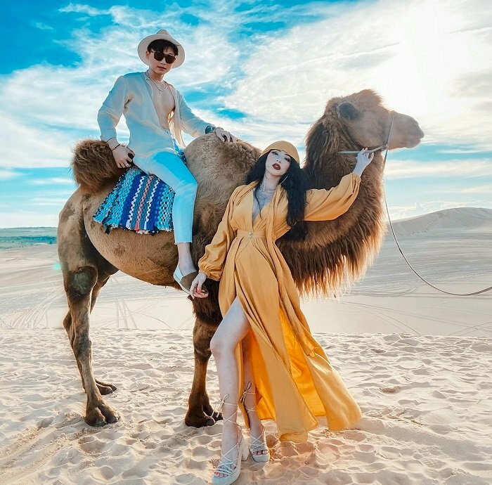 Cách tạo dáng chụp ảnh trên đồi cát cho đôi nam nữ cạnh con lạc đà, với dáng này nam hãy ngồi lên lạc đà, nữ đứng dưới, 1 tay cầm lên dây dẫn lạc đà, đứng trụ trên 1 chân và đưa 1 chân lên phía trước, đầu hơi nghiêng về 1 bên.