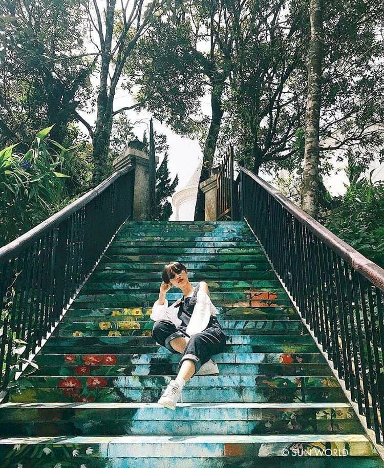 Cách tạo dáng chụp ảnh ở con đường bích họa ngầu chất bằng cách ngồi trên bậc thang, đặt xéo 1 chân đưa thẳng ra, 1 chân cho lại, người nghiêng về 1 bên, đưa 1 tay lên chóng trên đầu. 