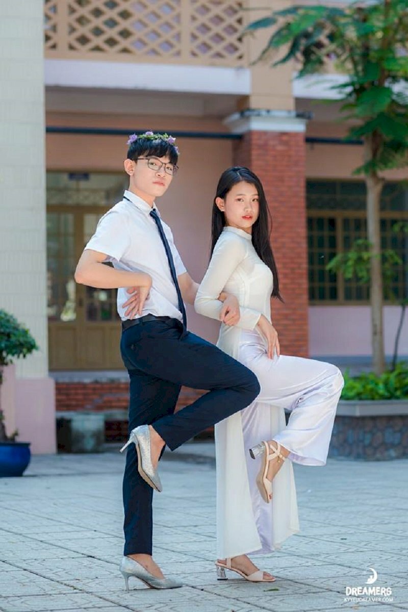 Cách tạo dáng chụp ảnh kỷ yếu đôi nam nữ vô cùng sáng tạo với góc chụp nghiêng, 2 bạn đưa tay lên chống hông và 1 chân co lên.