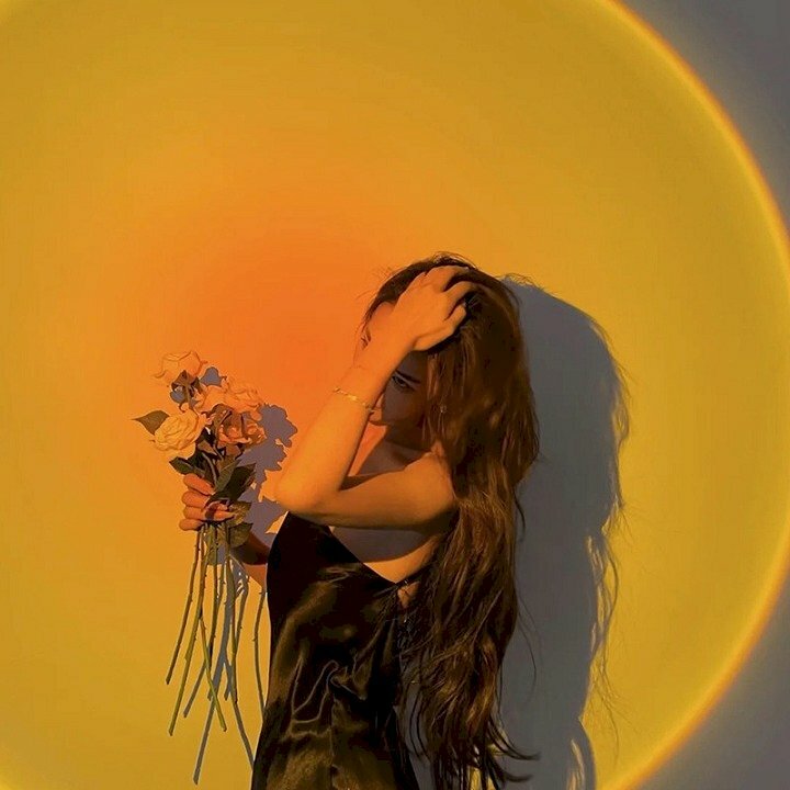 Cách tạo dáng chụp ảnh tại nhà với đèn Led cực đơn giản với dáng đứng nghiêng người về phía ống kính, 1 tay cầm bó hoa và tay còn lại đưa nhẹ lên vuốt tóc.