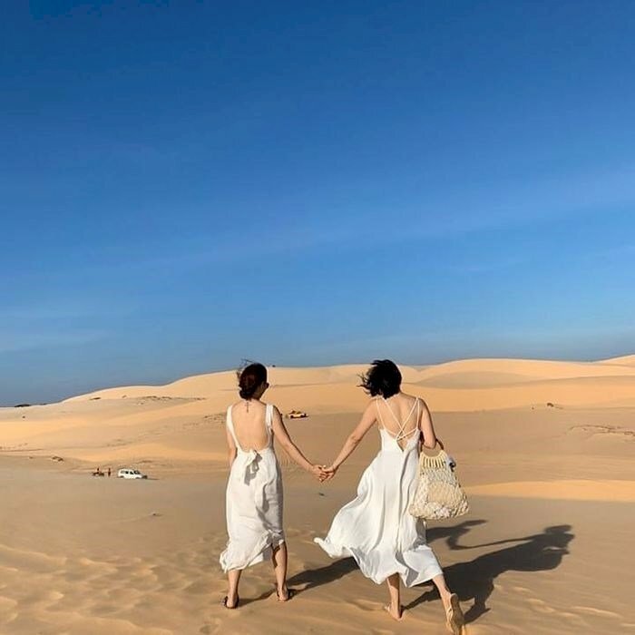 Cách tạo dáng chụp ảnh trên đồi cát cho đôi bạn thân nữ, đang nắm tay nhau đi trên đồi cát.  