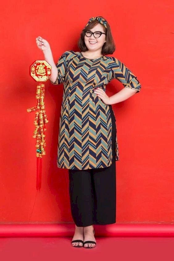 Cách tạo dáng với áo dài cho người béo với phụ kiện dây pháo trang trí tết, nàng mập có thể đứng hơi nghiêng người, trụ lên 1 chân, 1 tay cầm dây pháo trang trí đưa lên, và 1 tay chống ngay hông.