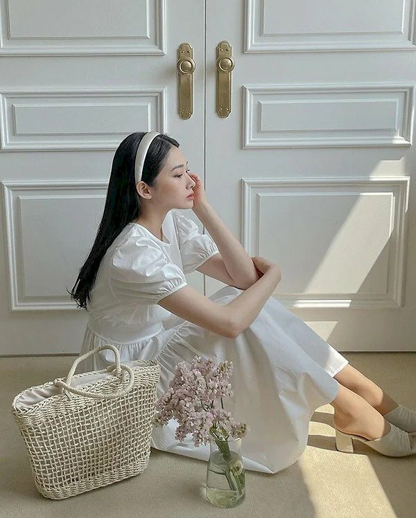 Cách tạo dáng với váy dài khi ngồi 1 tay đặt lên đầu gối, 1 tay chống cằm.