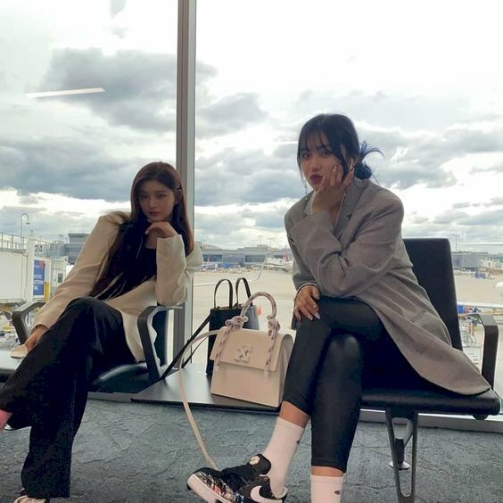 Cách tạo dáng chụp ảnh ở sân bay cho hai bạn nữ sang chảnh khi ngồi ở phòng chờ với dáng ngồi bắt chéo chân, đưa một tay lên chống cằm, người nghiêng nghiêng về một bên.