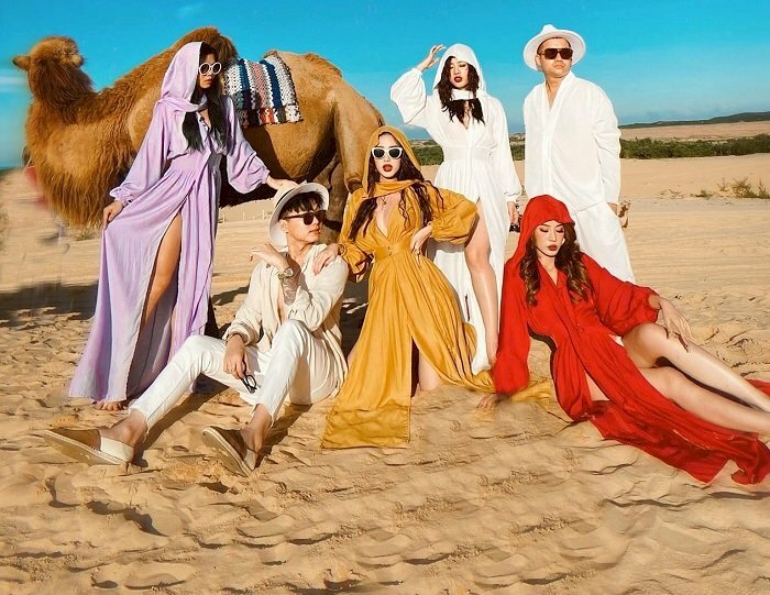 Cách chụp ảnh trên đồi cát cho nhóm bạn thân 6 người cùng tạo dáng bên con lạc đà, có 2 người ngồi trên cát, 1 người quỳ trên cát và 3 người đứng trên cát.