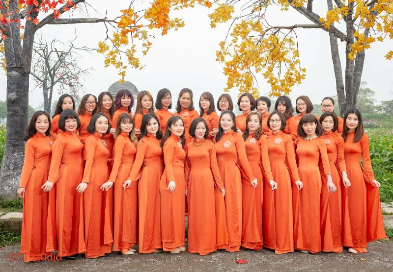 Cách tạo dáng chụp ảnh áo dài tập thể kiểu tập thể đoàn kết với nhóm trên 20 người, cùng xếp thành 2 hàng, hàng trước mọi người đứng xoay nghiêng người vào trung tâm, tay cầm nhẹ tà áo dài sau đưa lên, còn hàng sau mọi người sẽ đứng lên bậc để cao hơi hàng trước và tay người này sẽ đặt nhẹ lên khuỷu tay người kia.