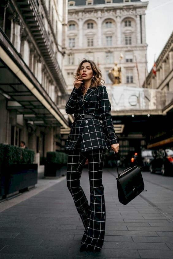 Cách tạo dáng chụp ảnh với vest nữ đang bước đi tung tăng trên phố, với 1 tay cầm túi xách, 1 tay để nhẹ lên cằm, một chân đằng sau co nhẹ, 1 chân đứng thẳng. 