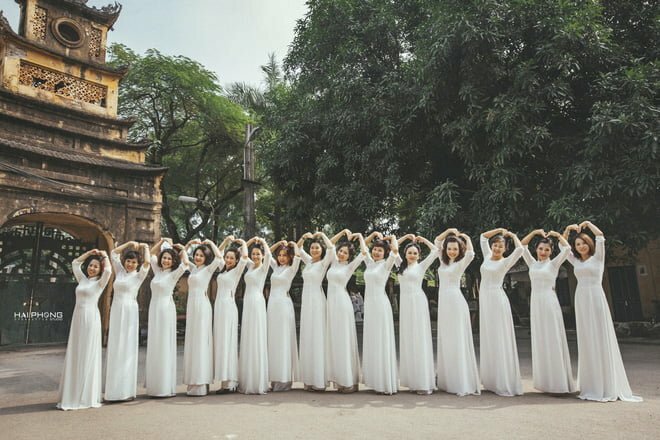 Cách tạo dáng chụp ảnh áo dài tập thể kiểu tập thể đoàn kết dành cho nhóm 15 người, mọi người cùng mặc áo dài trắng, xếp hàng ngang tạo hình vòng cung, cùng nhau đưa tay lên đầu tạo hình trái tim.