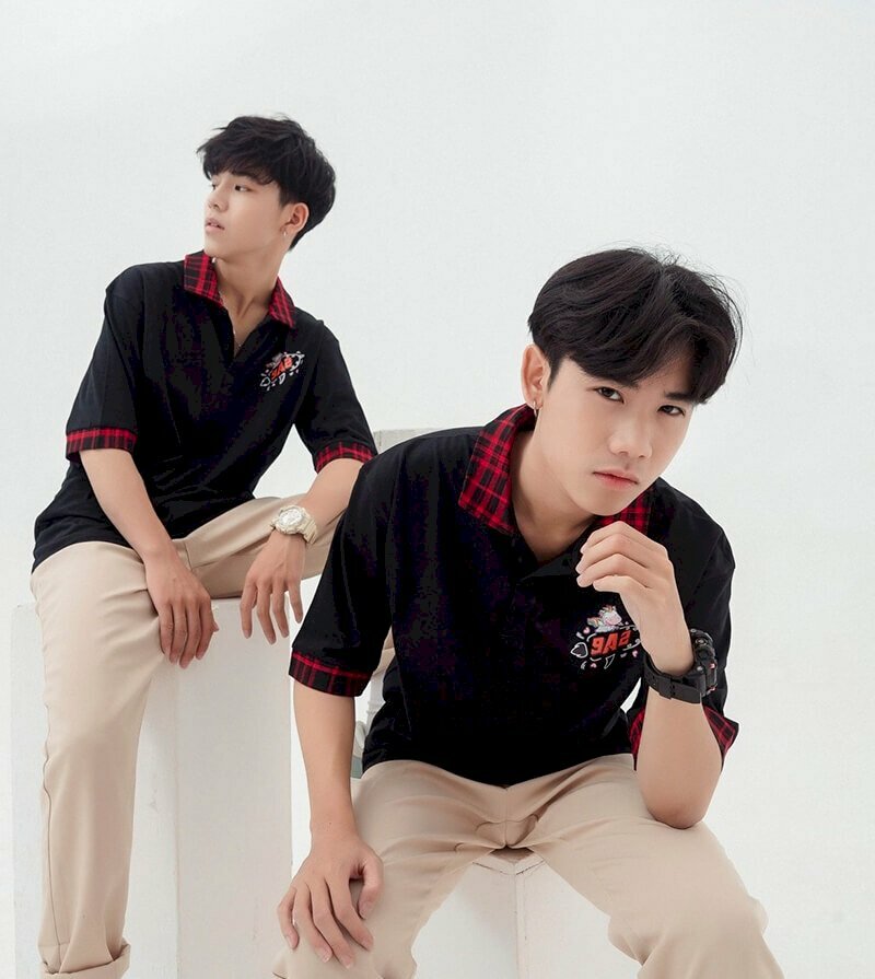 Cách tạo dáng chụp ảnh kỷ yếu đôi nam học sinh với biểu cảm ngầu chất khi ngồi trên ghế, với 1 bạn ngồi ghế thấp người khom xuống, đưa tay lên chống cằm và 1 bạn ngồi ghế cao, chân để rộng thoải mái, với 1 chân đặt trên cao, tay chống trên chân, đang quay đi nhìn về hướng khác.