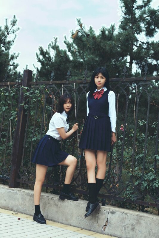 Cách tạo dáng chụp ảnh đôi nữ cực ngầu với 1 bạn đứng lên hàng tường rào đứng thẳng chân bắt chéo, 1 bạn đứng dưới bỏ 1 chân lên hàng rào, đang quay vào.