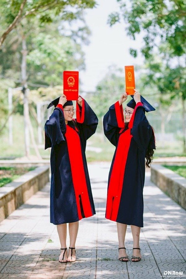 Cách tạo dáng chụp ảnh áo cử nhân kỷ yếu đôi nữ, hai bạn cùng đứng thẳng và quay mặt vào nhìn nhau cười tươi, tay cầm bằng tốt nghiệp đưa lên trên đầu.