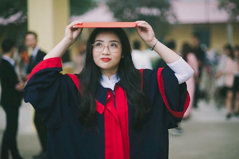 Kiểu tạo dáng siêu dễ thương cho các bạn nữ với kiểu đứng thẳng, 2 tay cầm bằng tốt nghiệp để trên đầu, miệng cười nhẹ, mắt nhìn hướng lên