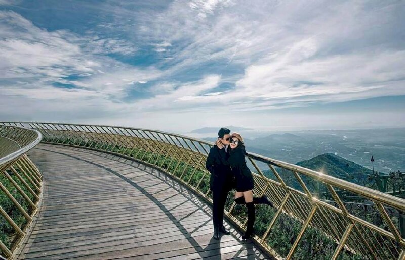 Tạo dáng chụp ảnh trên cầu khi đi du lịch của cặp tình nhân diện đồ màu đen tuyệt đẹp với tư thế cô gái ôm cổ chàng trai, đứng co một chân miệng cười tươi, mắt mang kính đen nhìn ống kính cùng chàng trai trong tư thế đứng thẳng hơi nghiêng người, tay đặt vào túi áo