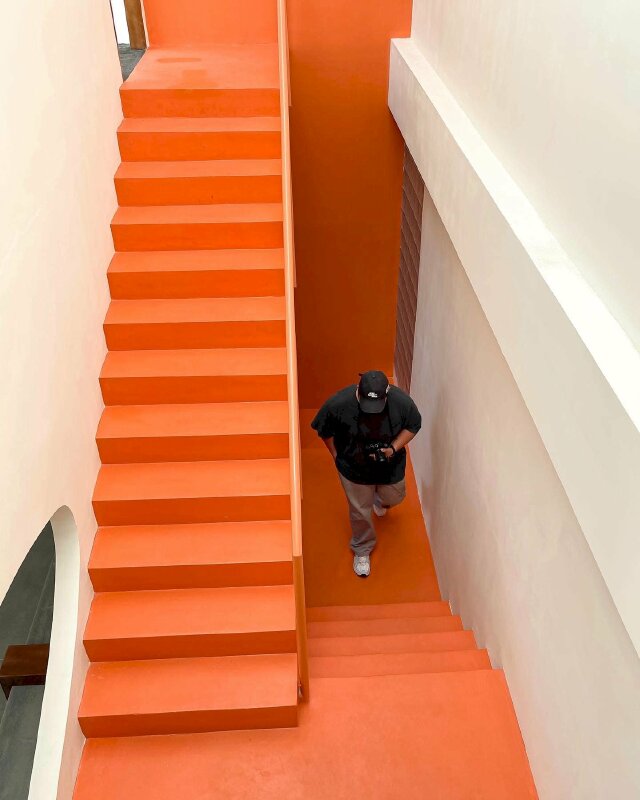 Cách tạo dáng nam đang đi lên cầu thang trong quán cafe trong bộ quần áo mang phong cách bụi, đầu đội mũ lưỡi trai, tay cầm điện thoại, tay còn lại bỏ vào quần, chụp từ góc phía trên xuống