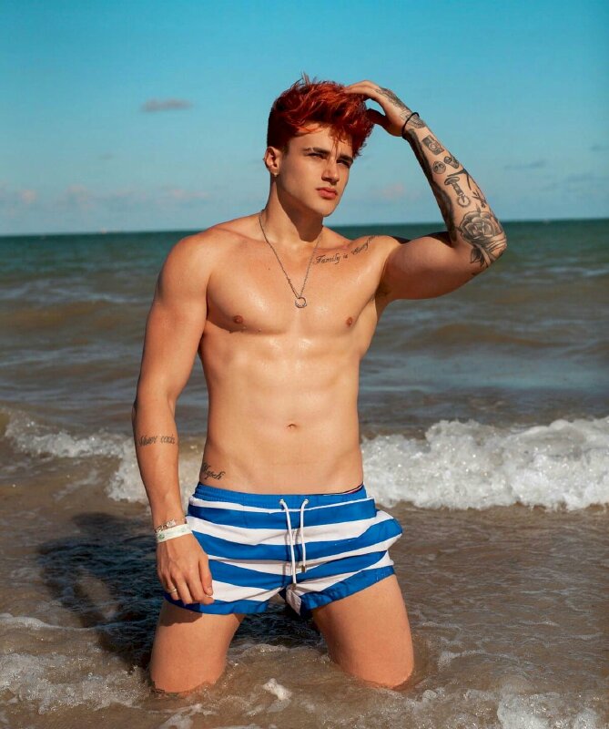 Cách tạo dáng nam thần giữa biển lộ cơ thể sáu múi, một tay để xuôi, tay còn lại chạm nhẹ tóc mặt nhìn hơi nghiêng