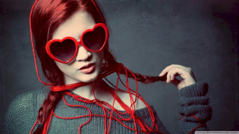 Kiểu tạo dáng cute đầy cá tính với mái tóc óng ánh đỏ thắt bím 2 bên cùng chiếc kính râm đỏ hình trái tim và áo len hở một bên vai, dáng người thẳng, một tay nắm đuôi tóc