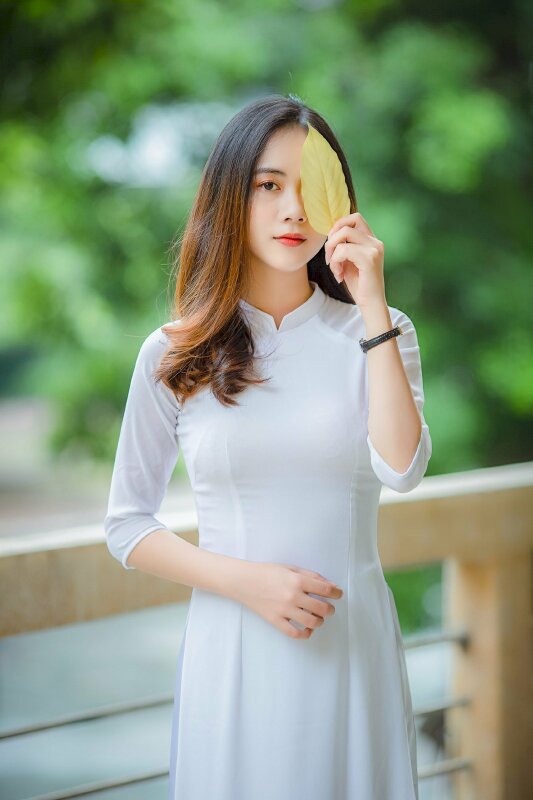 Kiểu tạo dáng dễ thương với 1 tay cầm chiếc lá che bên mắt tay còn lại co trước bụng, dáng đứng thẳng tự nhiên