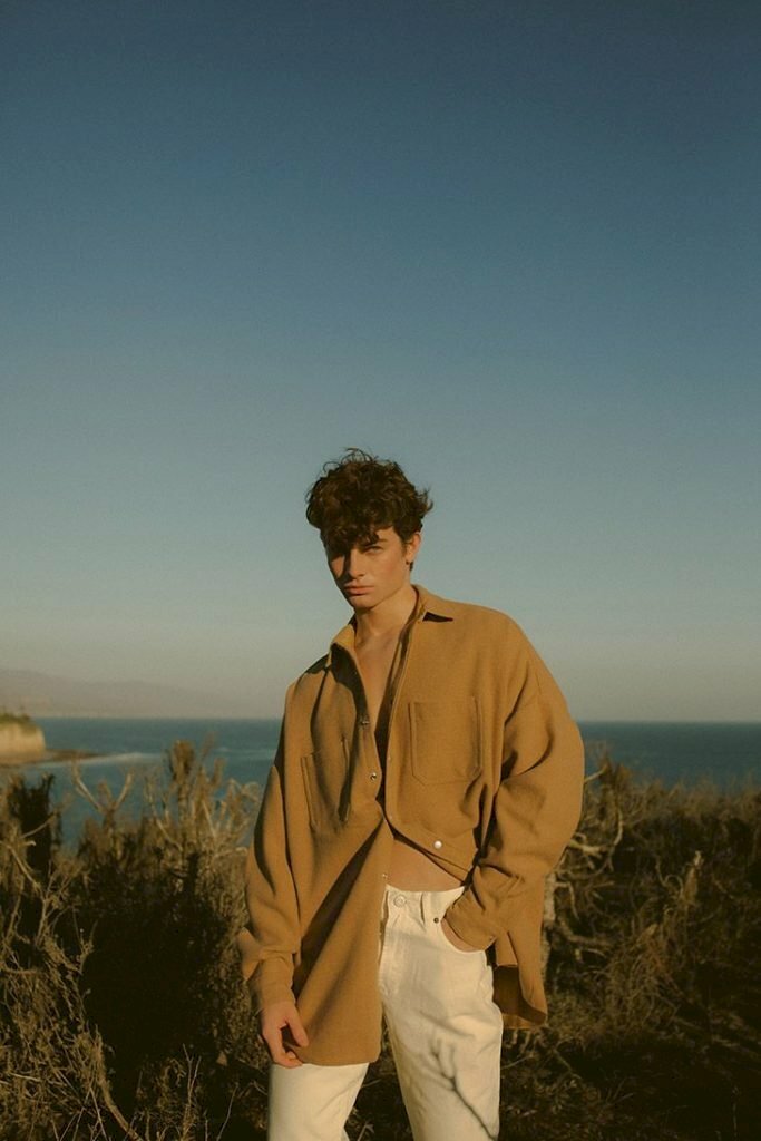 Kiểu tạo dáng nam với chiếc áo sơ mi một bên thả xuống một bên vén lên, một tay bỏ vào quần vẻ mặt nam tính dưới bầu trời nắng nhạt