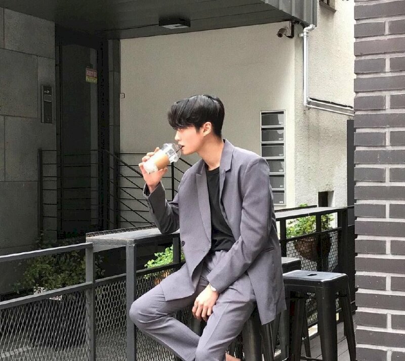 Kiểu tạo dáng ngồi uống cafe cuốn hút cho nam trong bộ áo vest xám, 1 tay cầm cốc cafe đưa lên môi, một tay chạm nhẹ đùi, chụp góc nghiêng tạo sự sang trọng