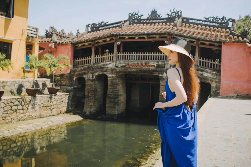 Cách tạo dáng khi đi chơi ở Hội An của cô gái trong chiếc đầm xanh dương tuyệt đẹp với dáng đứng nghiêng, 1 tay nắm lấy váy áo, mặt quay nghiêng nhìn xa xăm