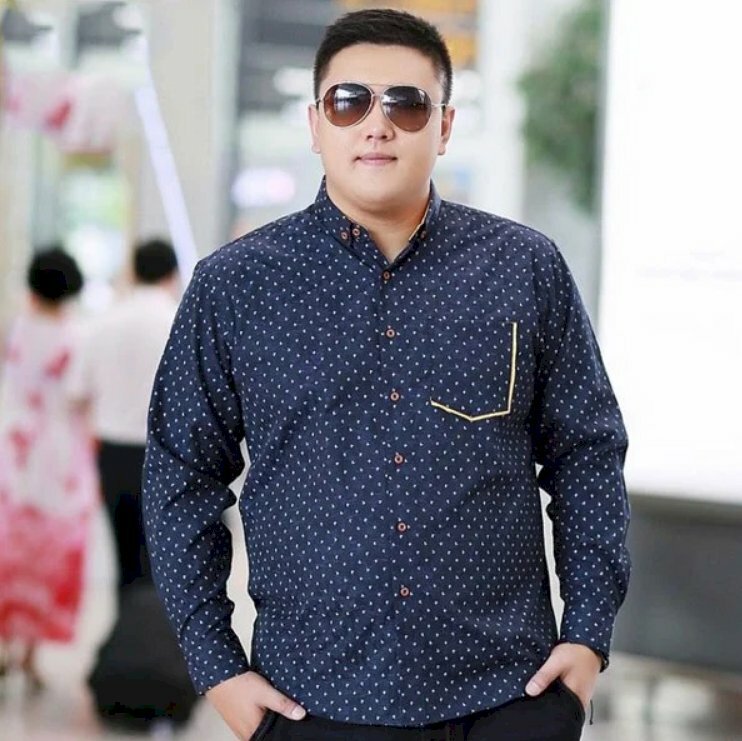 Tạo dáng nam tính trong chiếc áo sơ mi xanh dương chấm bi với 2 tay đặt túi quần, miệng cười mìm cùng chiếc kính râm chất ngầu