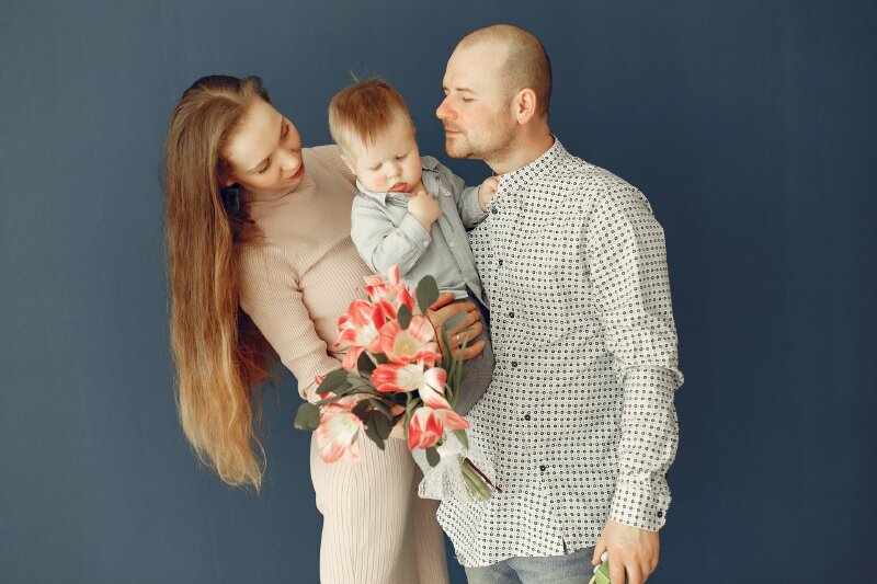 Tạo dáng chụp ảnh gia đình 3 người trên nền phông xanh dương, tay bố ẵm con, cùng người vợ bế con cực hạnh phúc